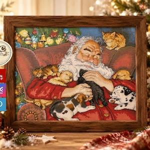 Puede incluir: Un bordado en punto de cruz enmarcado que representa a Santa Claus con barba blanca y ropa roja, durmiendo en un sillón rodeado de varios gatitos y cachorros pequeños. La escena incluye un árbol de Navidad decorado al fondo.