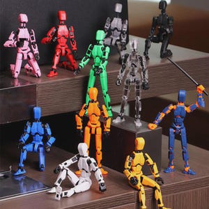 Könnte beinhalten: Eine Sammlung von beweglichen Actionfiguren in verschiedenen Farben, darunter Rosa, Rot, Grün, Orange, Blau, Weiß, Schwarz, Transparent und Gelb. Die Figuren sind in verschiedenen Positionen dargestellt, einige stehen, knien oder sitzen. Eine Figur hält ein kleines Schwert.