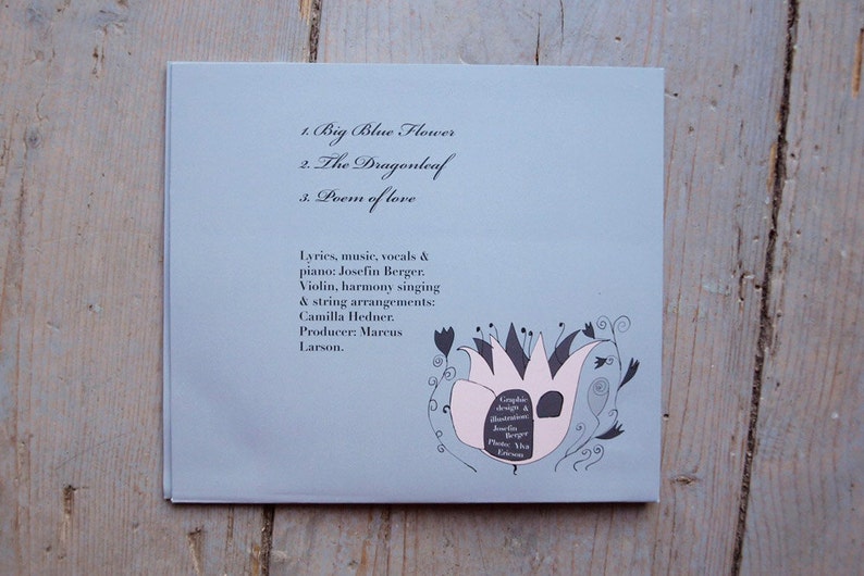 May include: A light blue CD cover with the title "Big Blue Flower" and the track list: "Big Blue Flower", "The Dragonleaf", and "Poem of Love". The cover features a black and white illustration of a flower with pink petals.