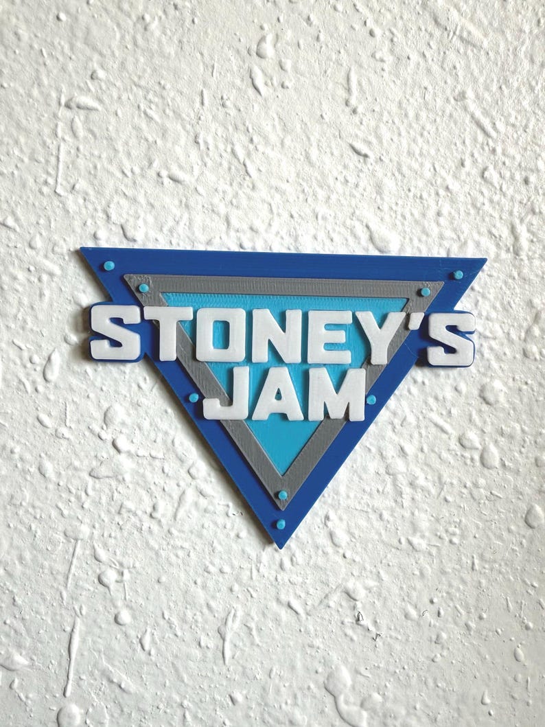 May include: A blue, gray, and white triangular sign with the text "STONEY'S JAM". The sign has a blue border with gray and light blue interior sections. The text is white and in a bold, sans-serif font.