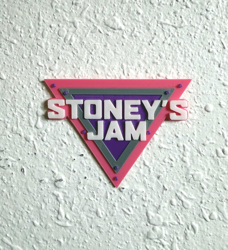May include: A triangular sign with the text "STONEY'S JAM" in white letters. The sign has a pink border, a gray middle section, and a purple center. Small, round, purple accents are visible on the corners.