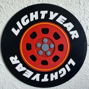 May include: A round black and red decorative piece with the text "LIGHTYEAR" in white. The design features a red wheel with a yellow outline and gray bolts, resembling a tire.
