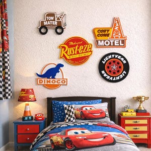 May include: A child's bedroom decorated with Cars movie theme. The room features a bed with a Lightning McQueen comforter, a bedside table with a lamp, and wall decor including signs and a Lightyear wheel.