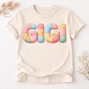 May include: Cream-colored t-shirt featuring the name "GIGI" in a patchwork design. The letters are composed of various fabrics in pastel colors, including pink, blue, yellow, and green, with floral and gingham patterns.