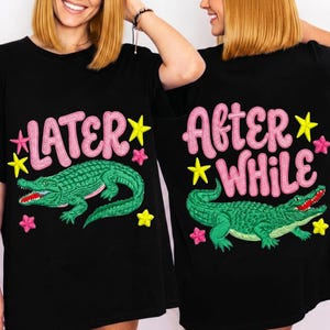 Puede incluir: Camisetas negras con diseños a juego. Una camiseta presenta el texto "LATER" sobre un caimán verde con boca roja, estrellas amarillas y flores rosas. La otra camiseta dice "AFTER WHILE" con un diseño de caimán similar.