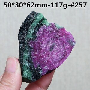 Op de afbeelding: Een ruwe edelsteen met een levendige kleurenmix. De steen heeft een diep magenta centrum, begrensd door groene en zwarte banden. De tekst op de afbeelding luidt: 50*30*62mm-117g-#257. Dit is een uniek mineraal specimen.