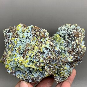 May include: A natural mineral specimen featuring a cluster of light blue, yellow, and brown crystals. The crystals are clustered together, creating a textured surface. The mineral is a unique and eye-catching piece.