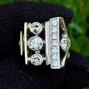 May include: A silver ring with three large, round diamonds and a vertical row of smaller diamonds. The ring has a unique, geometric design with a rectangular shape and a curved band. The diamonds sparkle against the silver setting.