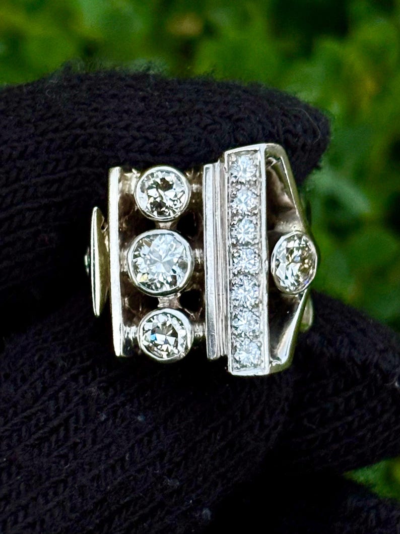 May include: A silver ring with three large, round diamonds and a vertical row of smaller diamonds. The ring has a unique, geometric design with a rectangular shape and a curved band. The diamonds sparkle against the silver setting.