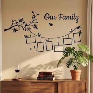 May include: A black wall decal featuring a tree branch design with the text Our Family, accompanied by five rectangular photo frames hanging from the branch, a small bird silhouette, and decorative leaves on a light beige wall.