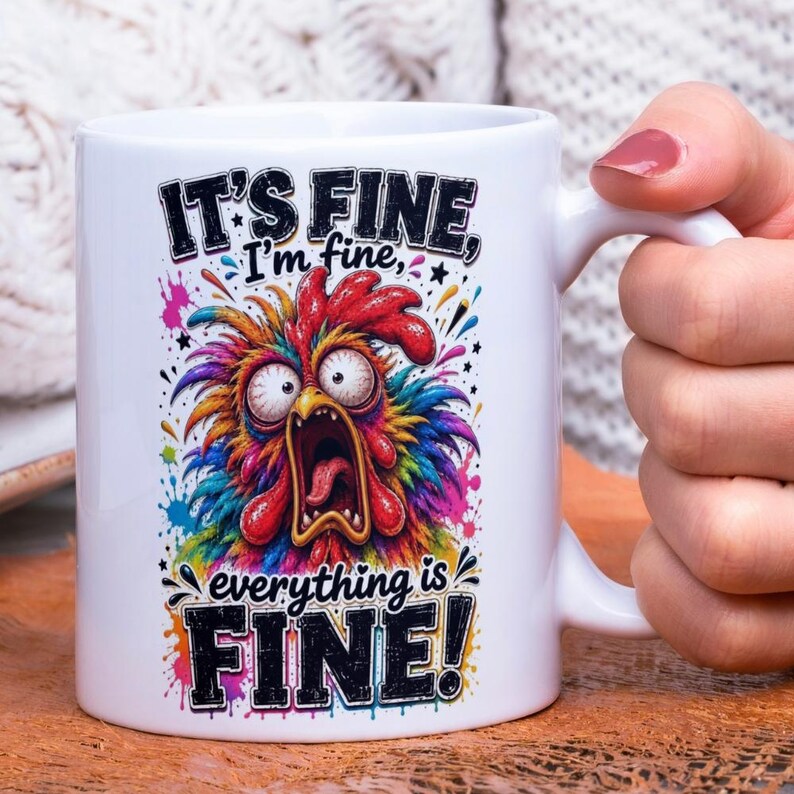 Op de afbeelding: Witte keramische mok met een kleurrijk cartoon haan ontwerp. De haan heeft een wijd open mond en grote ogen. De mok heeft de tekst "IT'S FINE, I'm fine, everything is FINE!" in zwart en wit.