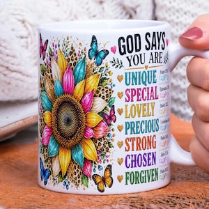 May include: White ceramic mug featuring a colorful sunflower design with butterflies and leopard print accents. The mug has the text "GOD SAYS YOU ARE UNIQUE SPECIAL LOVELY PRECIOUS STRONG CHOSEN FORGIVEN".