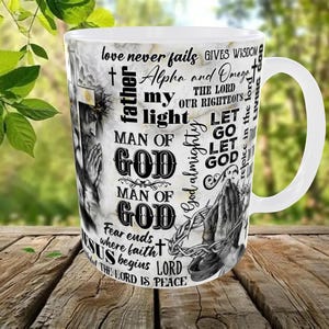 May include: White ceramic mug with a marble-like background and religious text and imagery. The mug features phrases like "love never fails" and "Man of God," along with an image of praying hands and a depiction of Jesus.
