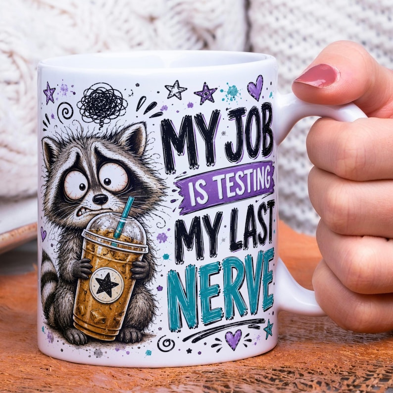 May include: A white ceramic mug featuring a cartoon raccoon holding an iced coffee. The text reads, "MY JOB IS TESTING MY LAST NERVE." The design includes purple and teal accents, small stars, and hearts, with a distressed, hand-drawn aesthetic.