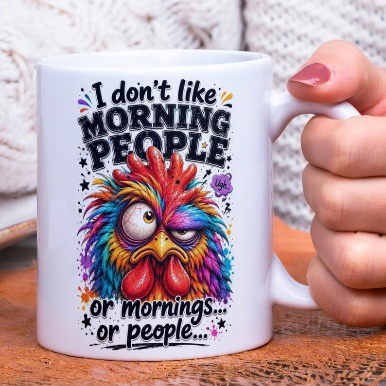 Op de afbeelding: Witte keramische mok met een kleurrijk, cartoonachtig hanenontwerp. De tekst op de mok luidt: "I don't like MORNING PEOPLE or mornings... or people..."