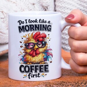 Op de afbeelding: Witte keramische koffiemok met een cartoon haan met een bril. De mok heeft de tekst "Do I look like a MORNING COFFEE first". De haan is geel, rood en blauw, met accenten van koffiebonen.