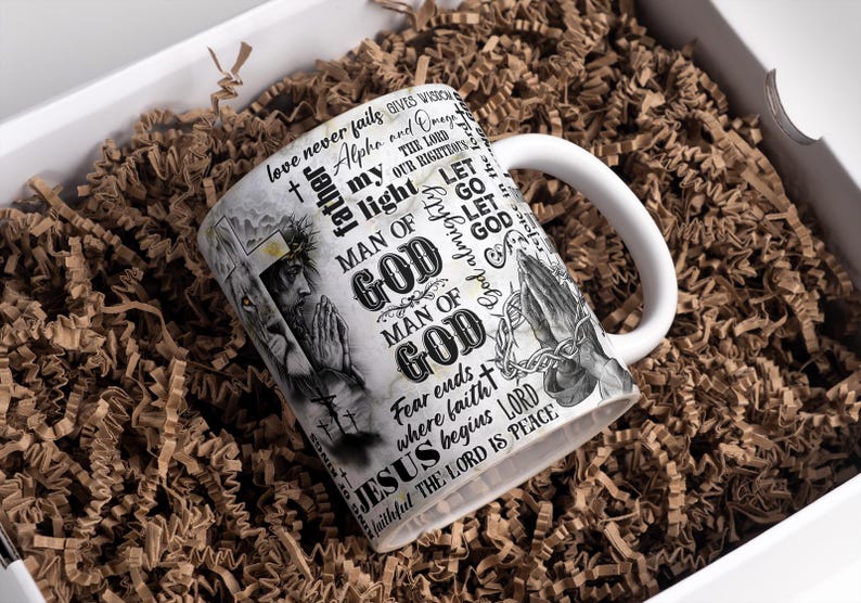May include: White ceramic mug with a wraparound design featuring religious imagery and text. The mug includes illustrations of praying hands, a figure with a crown of thorns, and the words "MAN OF GOD" and "JESUS". The mug is in a white gift box with brown paper filler.