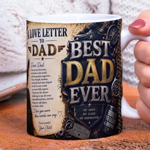 Op de afbeelding: Een witte keramische mok met een handvat, met een ontwerp met de tekst "A Love Letter to Dad" en "Best Dad Ever" in goud en zwart. De mok bevat een oprecht bericht en decoratieve elementen.