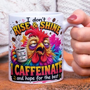May include: White ceramic coffee mug with a colorful rooster design. The mug features the text "I don't RISE & SHINE, I CAFFEINATE and hope for the best." A smaller mug graphic says "Powered by CAFFEINE & CHAOS."