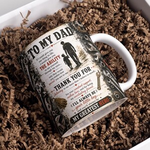 May include: A white ceramic mug with a handle, featuring a design with the text "TO MY DAD" and a silhouette of a father and child. The mug is in a white gift box filled with brown paper. The mug is approximately 4 inches tall.