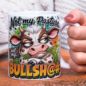 May include: White ceramic mug featuring a grumpy cow illustration with the text "Not my Pasture" and "BULLSH@#". The cow is brown and white with green eyes, eating grass. The mug has a white handle.