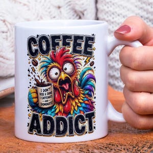 Op de afbeelding: Witte keramische koffiemok met een kleurrijk cartoon haan ontwerp. De mok heeft de woorden "COFFEE ADDICT" en de zin "I DON'T RISE & SHINE I CAFFEINATE -AND- DOMINATE!" in zwarte letters. De haan heeft grote ogen en een open bek.