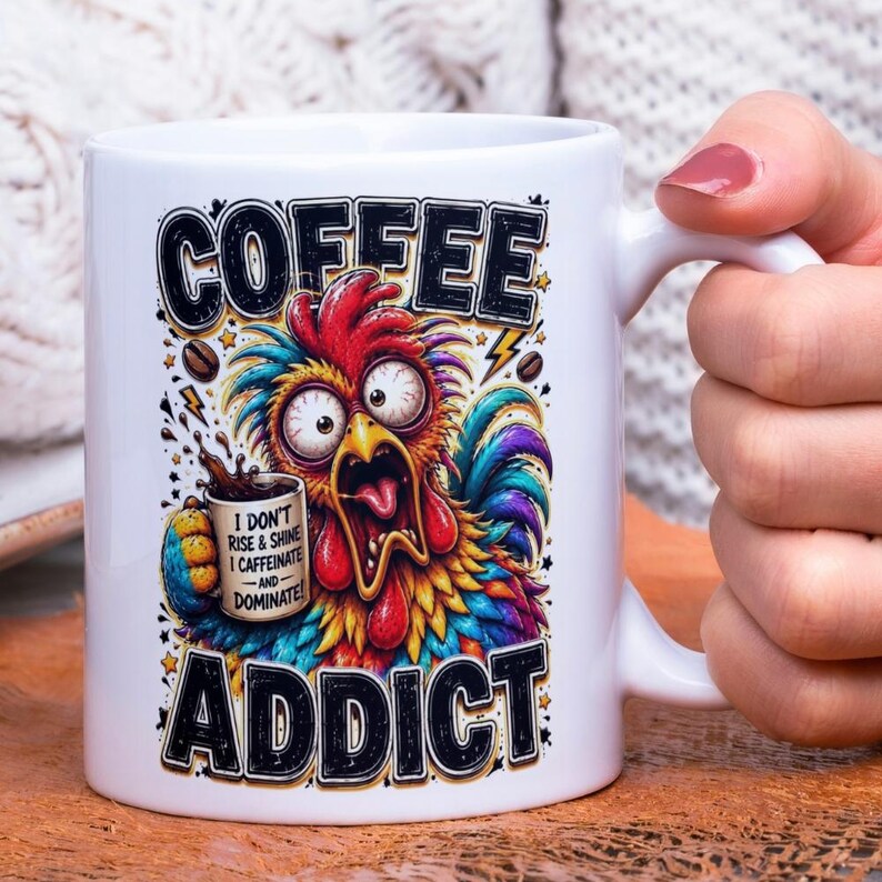 Op de afbeelding: Witte keramische koffiemok met een kleurrijk cartoon haan ontwerp. De mok heeft de woorden "COFFEE ADDICT" en de zin "I DON'T RISE & SHINE I CAFFEINATE -AND- DOMINATE!" in zwarte letters. De haan heeft grote ogen en een open bek.