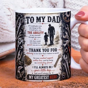May include: White ceramic mug with a handle, featuring a design dedicated to a father. The mug has a rustic, vintage aesthetic with text that reads "TO MY DAD" and a heartfelt message. The design includes illustrations of tools and a father and son walking together.