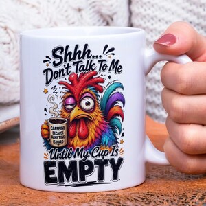 Op de afbeelding: Witte keramische mok met een kleurrijke haan illustratie en de tekst "Shhh... Don't Talk To Me Until My Cup Is EMPTY." De haan houdt een koffiekopje vast met de tekst "CAFFEINE BECAUSE ADULTING IS HARD."