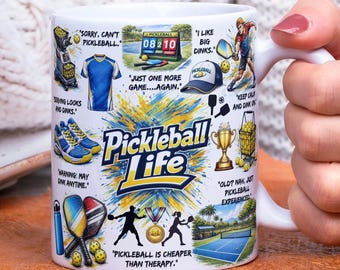May include: White ceramic mug with a wraparound design featuring pickleball-themed graphics and text. The mug includes illustrations of pickleball equipment, a court, and phrases like "Pickleball Life" and "Pickleball is cheaper than therapy."