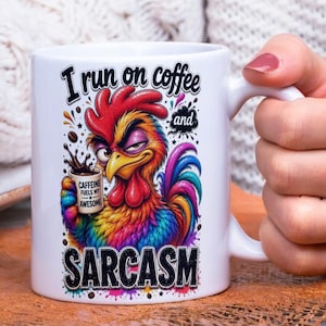Op de afbeelding: Witte keramische mok met een kleurrijke haan illustratie. De haan houdt een koffiekopje vast en de mok leest "I run on coffee and sarcasm". De haan is rood, geel, blauw en paars.