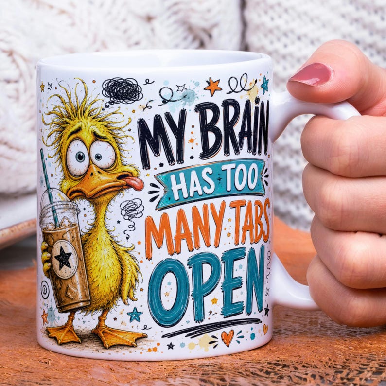 May include: A white ceramic mug featuring a cartoon yellow duck with messy hair holding an iced coffee. The text reads MY BRAIN HAS TOO MANY TABS OPEN in black, orange, and teal lettering, surrounded by small star and scribble illustrations.