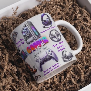 May include: White ceramic mug with a Gamer Life theme. The mug features gaming-related graphics, including a headset, controller, and computer. Text includes "Game On, Level Up!", "Eat, sleep, game, repeat."