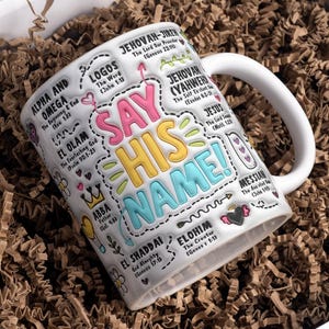 May include: White ceramic mug with the words "SAY HIS NAME!" in colorful bubble letters. The mug is decorated with various religious terms and phrases, including "Alpha and Omega" and "Jehovah-Jiren". The mug is presented in a box with brown paper filler.