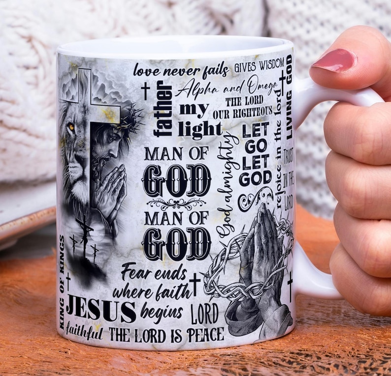 May include: White ceramic mug featuring religious imagery and text. The design includes a lion, a praying figure, and the words "Man of God," "Jesus," and other inspirational phrases. The mug has a white handle.