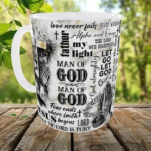 May include: White ceramic mug with a wraparound design featuring religious imagery and text. The design includes a depiction of Jesus, praying hands, and phrases like "Man of God" and "The Lord is Peace."
