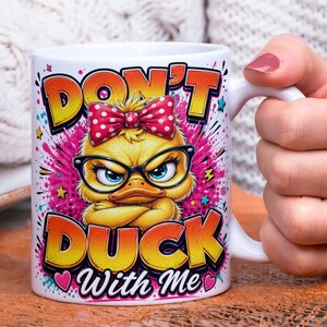 May include: White ceramic mug featuring a cartoon duck wearing glasses and a bow. The mug has the text "DON'T DUCK WITH ME" in orange and yellow lettering. The duck is set against a pink and purple splash design.