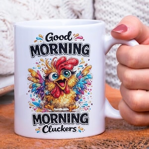 Op de afbeelding: Witte keramische mok met een kleurrijk cartoon haan ontwerp. De mok heeft de woorden "Good Morning" en "Morning Cluckers" in zwarte tekst. De haan heeft een rode kam, gele lichaam en regenboogkleurige vleugels.