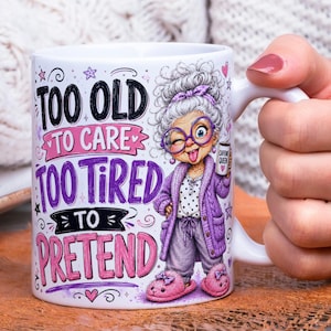 May include: A white ceramic mug featuring a cartoon illustration of an elderly person with gray hair, purple glasses, a purple cardigan, and pink slippers. The text reads: TOO OLD TO CARE, TOO TIRED TO, PRETEND, and CAFFEINE QUEEN on a small mug.