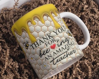 May include: White ceramic mug with a honeycomb and dripping honey design. The mug features the text "THANK YOU for bee-ing an AMAZING teacher" with bee and flower illustrations. The mug is packaged in a white box with brown paper filler.
