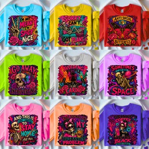 May include: A collection of nine colorful sweatshirts featuring various graphic prints including skeletons, butterflies, and text such as I'm Not Mean I'm Spicy Nice, Sorry Can't Got Plans, Anti-Social Butterfly, Go Away I'm Introverting, and Drinks Coffee.