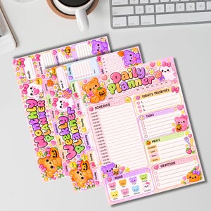 Pode incluir: Um conjunto de três planejadores de papel incluindo um Daily Planner, Weekly Planner e Monthly Planner. Cada folha é decorada com ilustrações coloridas de ursos, fantasmas, abóboras e doces em tons pastel com texto impresso.
