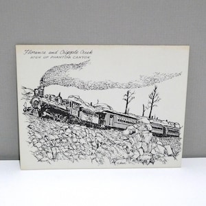 May include: Black and white illustration of a train traveling through a rocky landscape. The image includes the text "Florence and Cripple Creek HIGH UP PHANTOM CANYON". The train is emitting a large cloud of smoke.