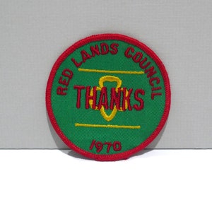 May include: A round, green patch with red trim and the words "RED LANDS COUNCIL" in red, arched around the top. The word "THANKS" is in red, with a yellow design below it. The year "1970" is at the bottom.
