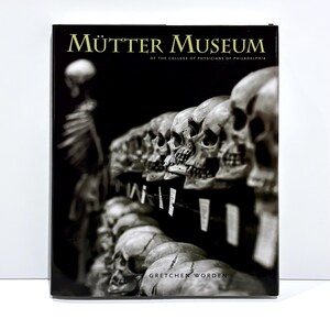 May include: A hardcover book titled Mütter Museum of the College of Physicians of Philadelphia by Gretchen Worden. The black cover features a high-contrast, monochromatic photograph of multiple human skulls arranged in rows with small white labels.