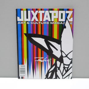 May include: A copy of Juxtapoz Art & Culture Magazine. The cover features the magazine's title in white block letters above the text "ART & CULTURE MAGAZINE". The background has vertical stripes of various colors. A black and white graphic is on the right.
