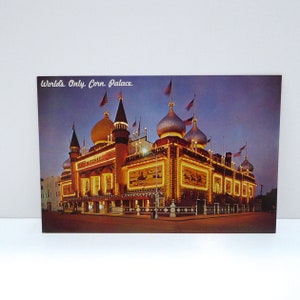 May include: Vintage postcard featuring the World's Only Corn Palace, a unique building with ornate domes and towers, illuminated with lights. The postcard has the text "World's Only Corn Palace" at the top. The building is a reddish-brown color with gold accents.