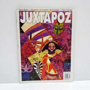 May include: A copy of Juxtapoz Art & Culture magazine. The cover features a collage of colorful tribal masks and figures, with the magazine's title in large, bold letters. The background is a mix of vibrant colors and abstract shapes.