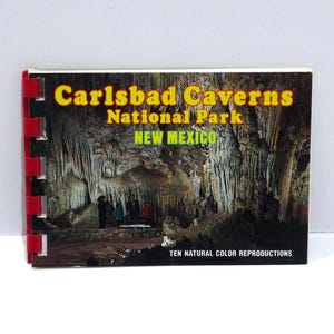 May include: A spiral-bound book featuring a photograph of Carlsbad Caverns National Park in New Mexico. The cover text reads "Carlsbad Caverns National Park" in yellow and "NEW MEXICO" in green. The image shows a cave interior with stalactites and people.