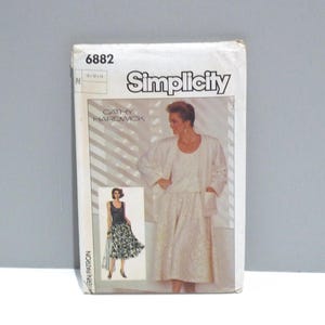 May include: A vintage Simplicity sewing pattern featuring a woman in a white outfit. The pattern includes a jacket, top, and skirt. The pattern number is 6882, and the designer is Cathy Hardwick.